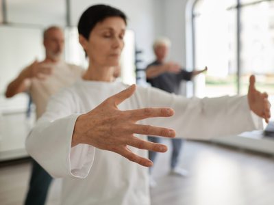 Medium shot with focus on hand of senior female student doing qigong concentration exercise in gym