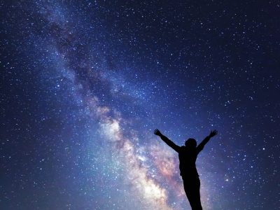 Milky Way. Night sky with stars and silhouette of a woman with raised-up arms.